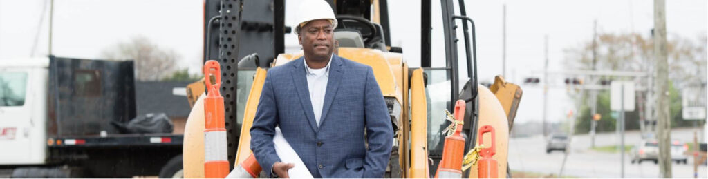 image of a black man wearing a nice suit and hard hat with plans under his arm